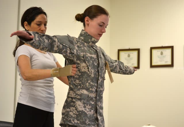 A woman in a military uniform demonstrates how to stretch her arm while modernizing her workwear.