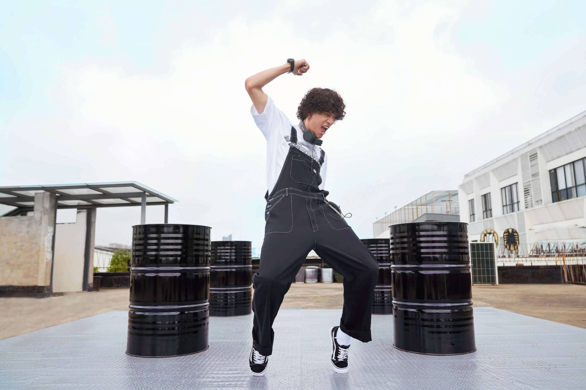 A man in Dickies overalls is dancing in front of barrels.