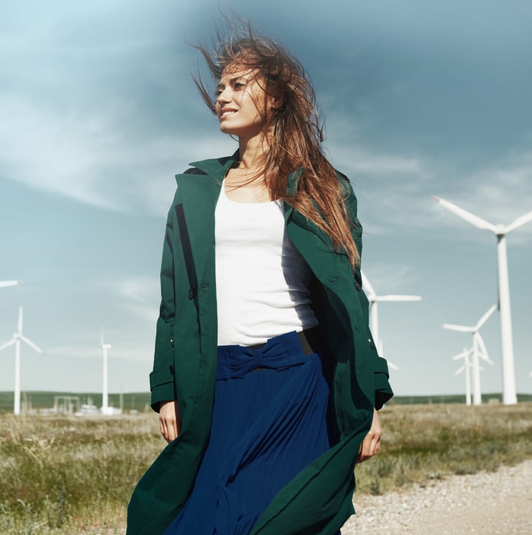 An influencer in a green coat is standing in front of wind turbines.