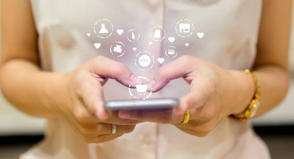 A woman's hand holding a smart phone with social icons, showcasing the latest trends in fashion eCommerce.