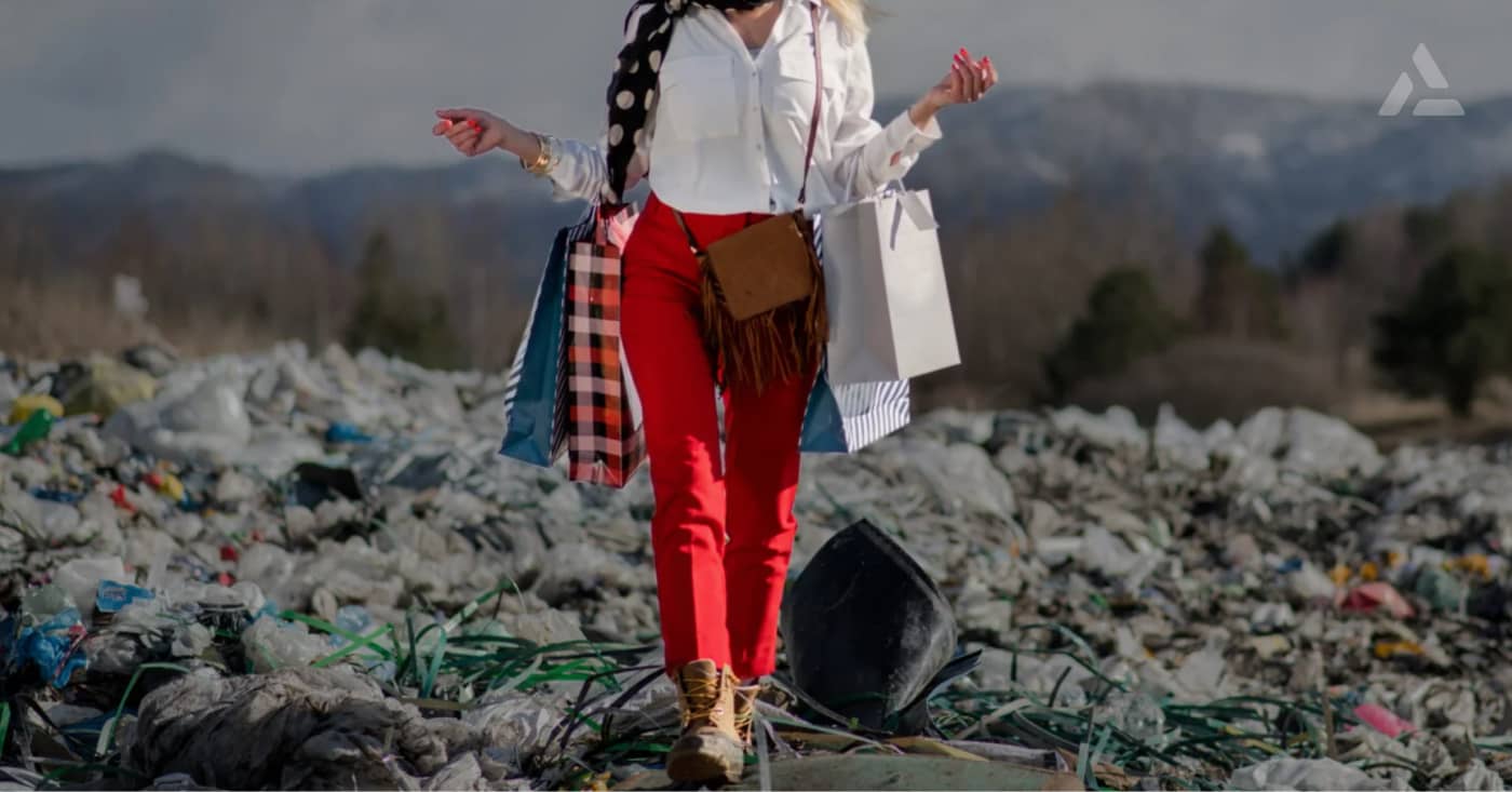 A woman in sustainable fashion attire balances on one leg atop garbage in a landfill, surrounded by a cloudy sky and distant mountains.