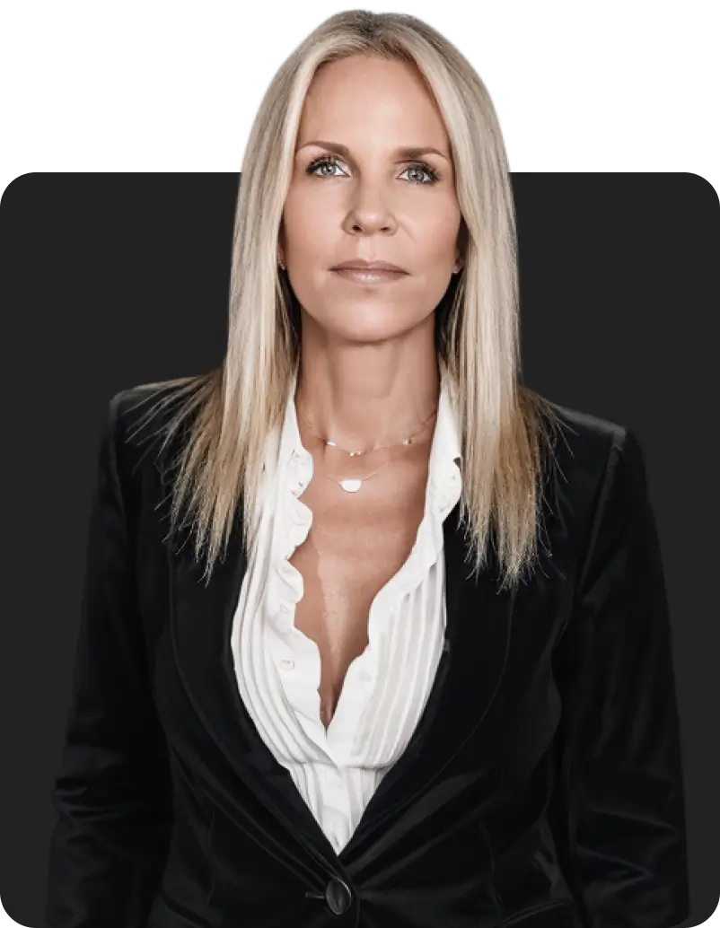 Professional portrait of a woman with long blonde hair, wearing a tailored black blazer and white blouse, set against a dark background.