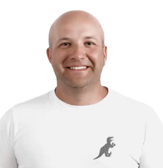 A smiling bald man wearing a white t-shirt with a lizard logo, stands against a black background for the "About Us" page.