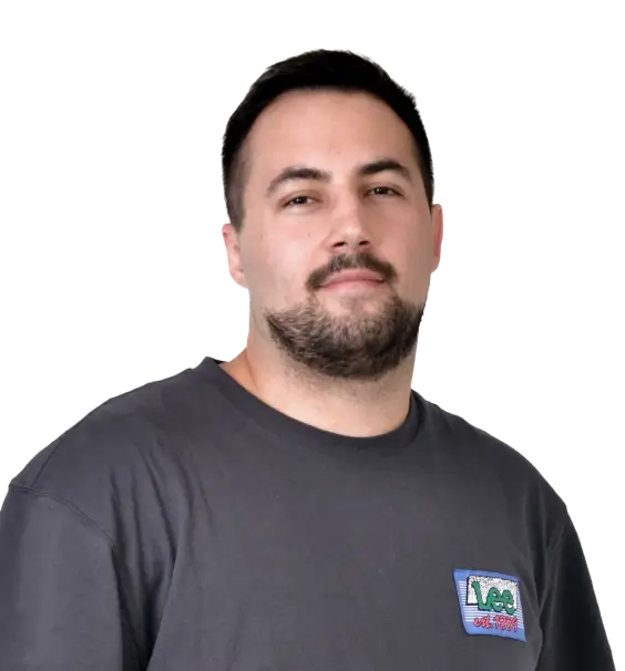 A man with a beard wearing a gray t-shirt with a small logo looks directly at the camera on a transparent background.