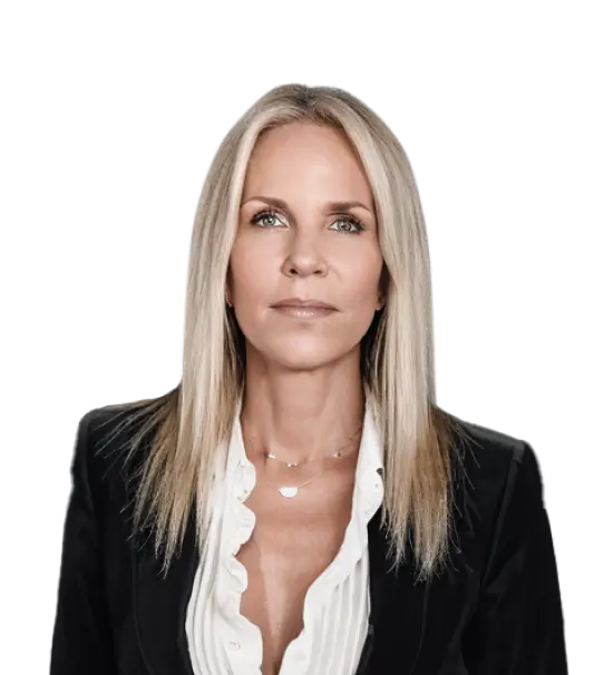 A portrait of a woman with long blonde hair, wearing a black jacket and white blouse, against a dark background.