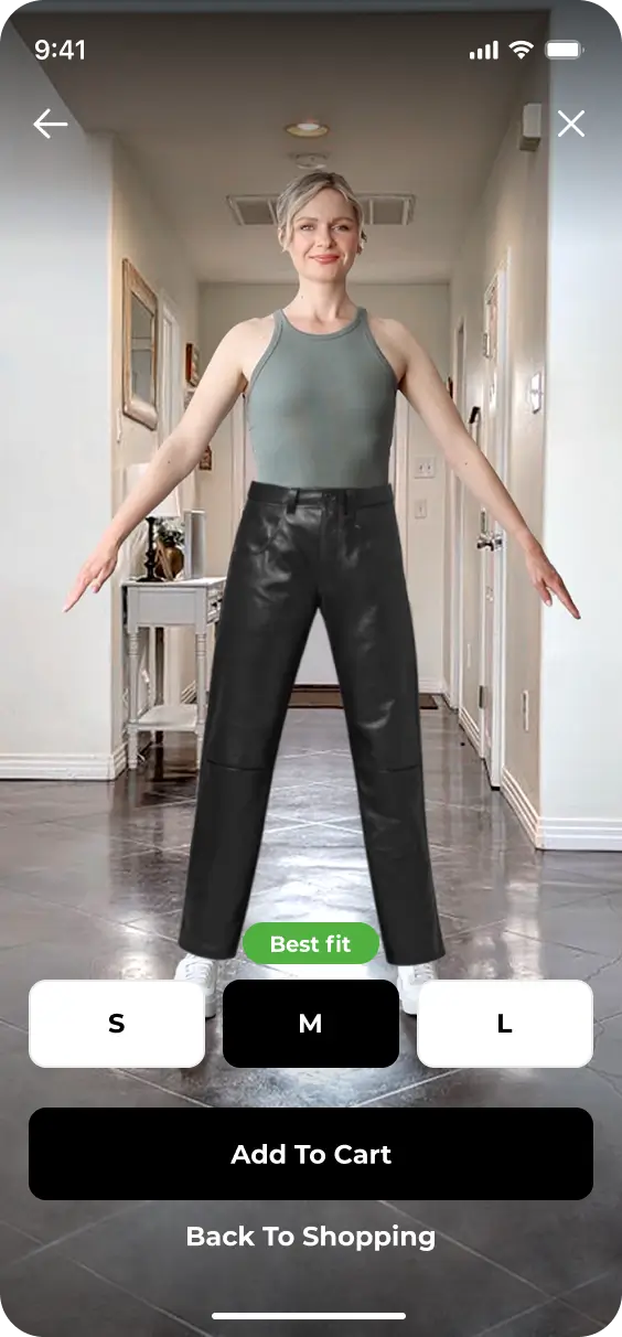 Person modeling a sleeveless gray top and black pants, standing with arms slightly open in a well-lit hallway. The screen shows size selection options, "Add To Cart" button, and the YourFit feature for the 2024 redesign.