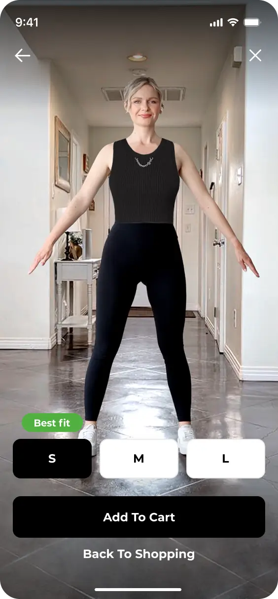 A person stands in a well-lit hallway modeling a black sleeveless top and black pants. With the YourFit feature, the screen displays size options (S, M, L) and buttons for "Add to Cart" and "Back to Shopping," making it easier than ever to find your perfect fit.