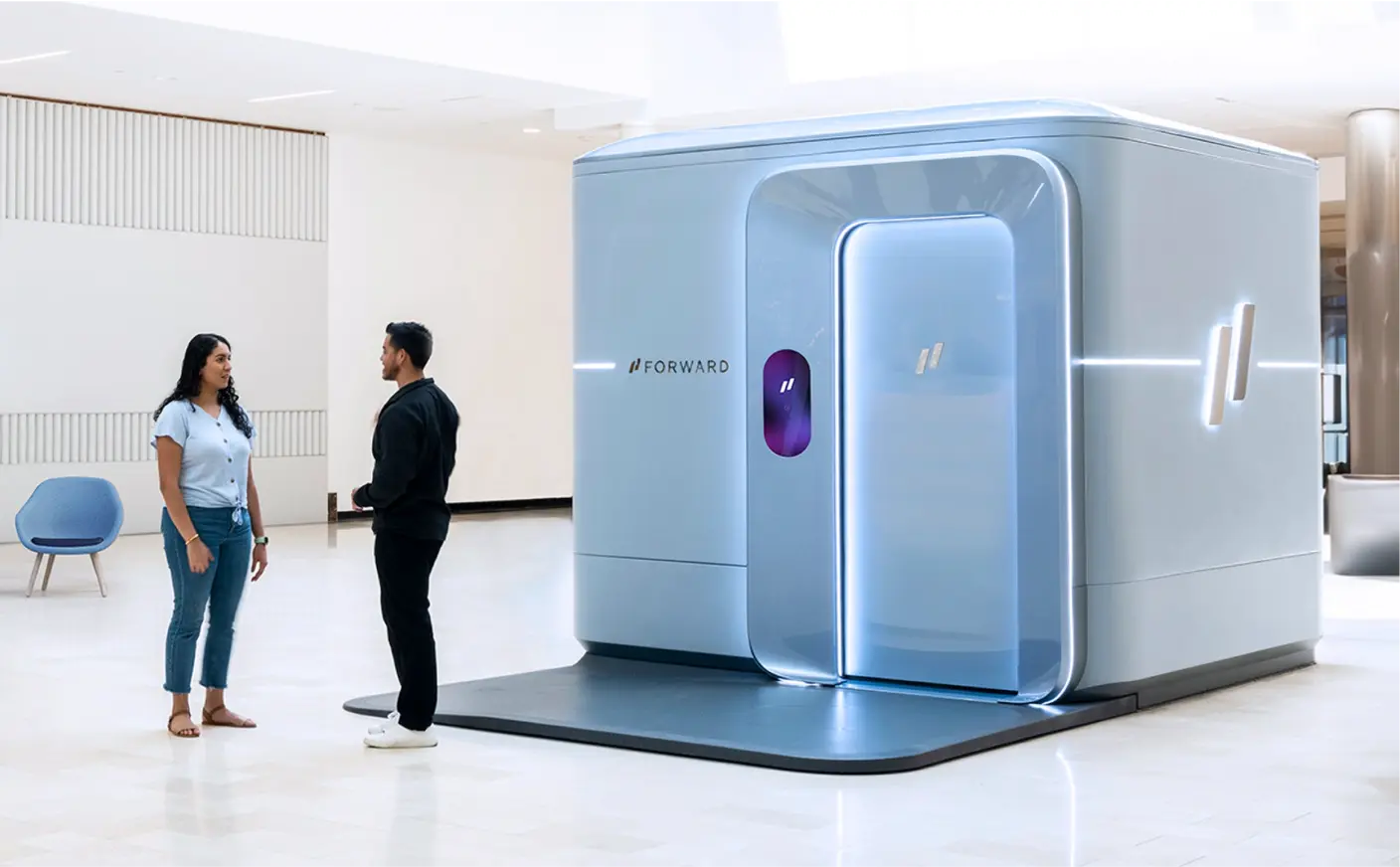Two people are standing and talking in front of a sleek, modern pod labeled "Forward" in a clean, spacious indoor area. The scene exudes the innovative spirit of health tech companies, hinting at the future of healthcare in 2024.