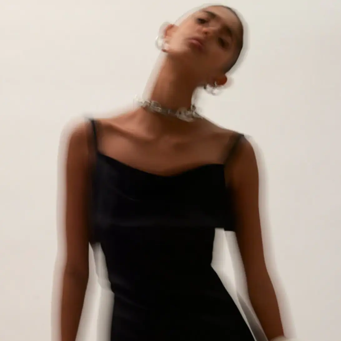 A person in a black dress with blurred motion stands against a plain background, showcasing the YourFit 2024 Redesign silver necklace and large earrings.