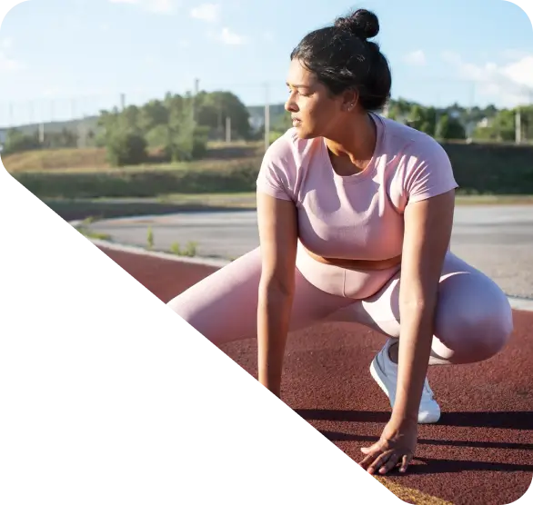 A person in a pink workout outfit kneels on the track, gazing sideways during their outdoor exercise—a scene that could grace any homepage.