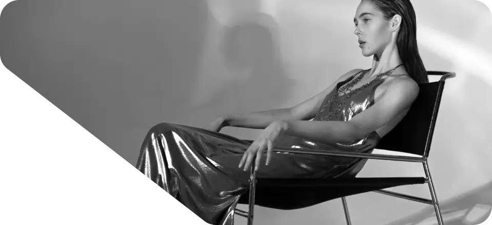 A person in a shiny dress reclines in a modern chair against a monochrome background, creating the perfect visual for a stylish homepage.