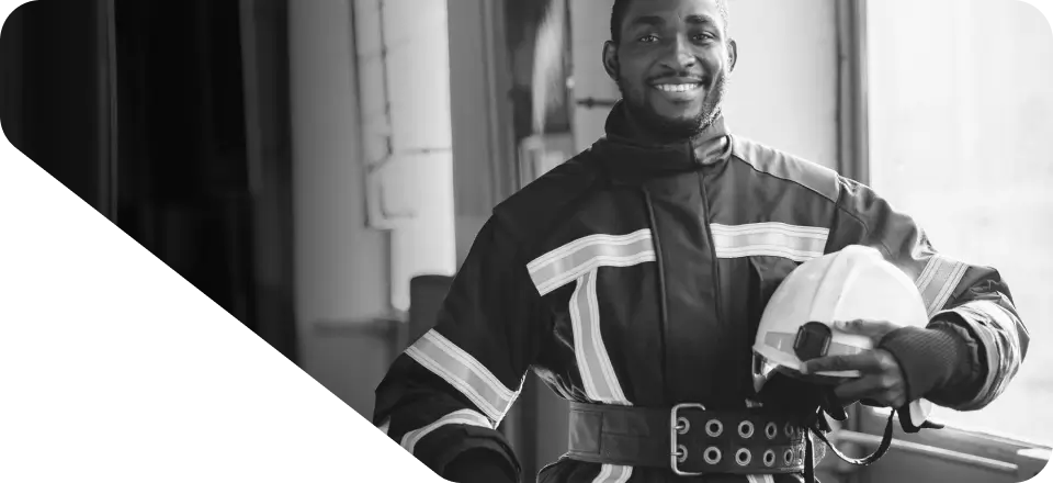 A person in a firefighter uniform stands indoors holding a white helmet, smiling at the camera—a perfect image for your website's homepage.