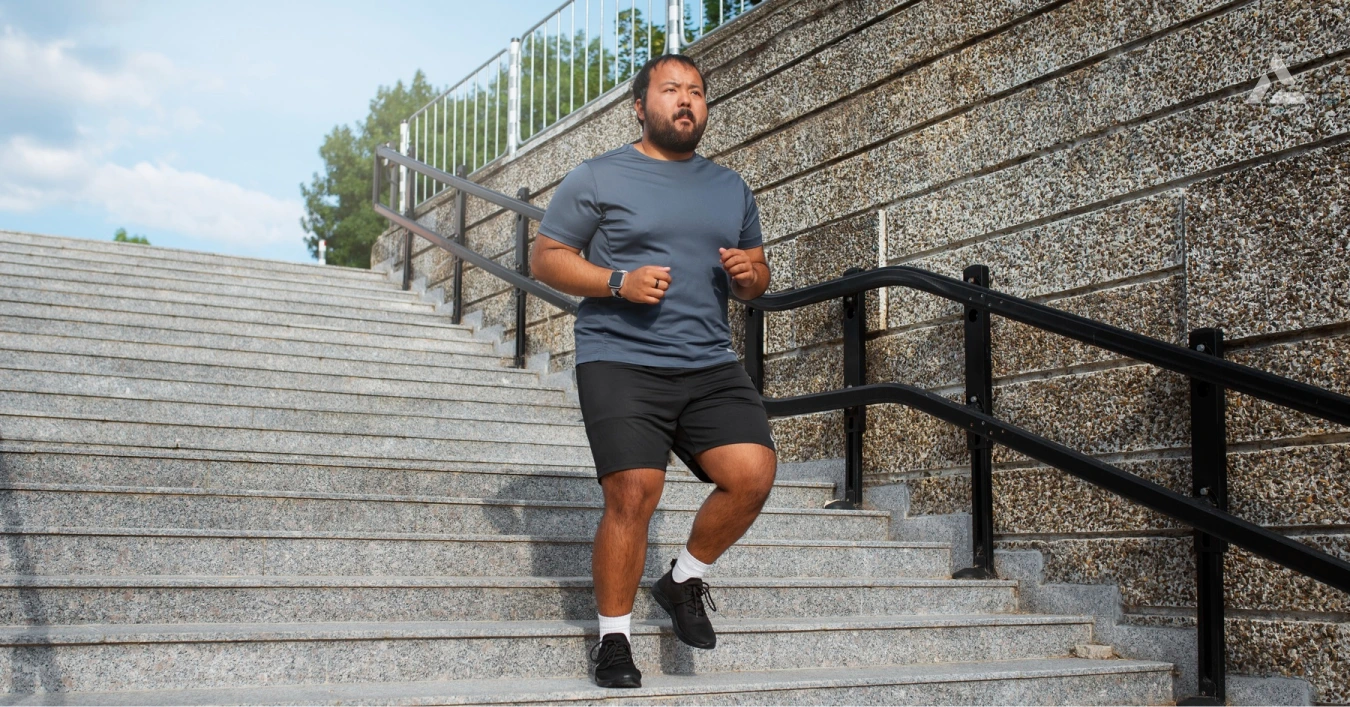 A man in athletic wear jogs up a set of outdoor concrete stairs, with a stone wall and black railings beside him—embodying the momentum shaping the fitness industry as it looks ahead to 2025.