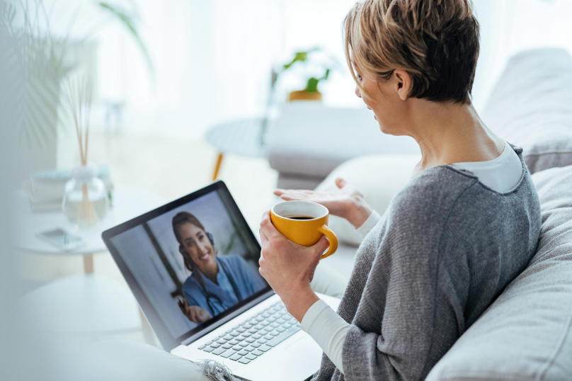 A person is sitting on a couch, holding a mug, and participating in a video call on their redesigned 2024 laptop.