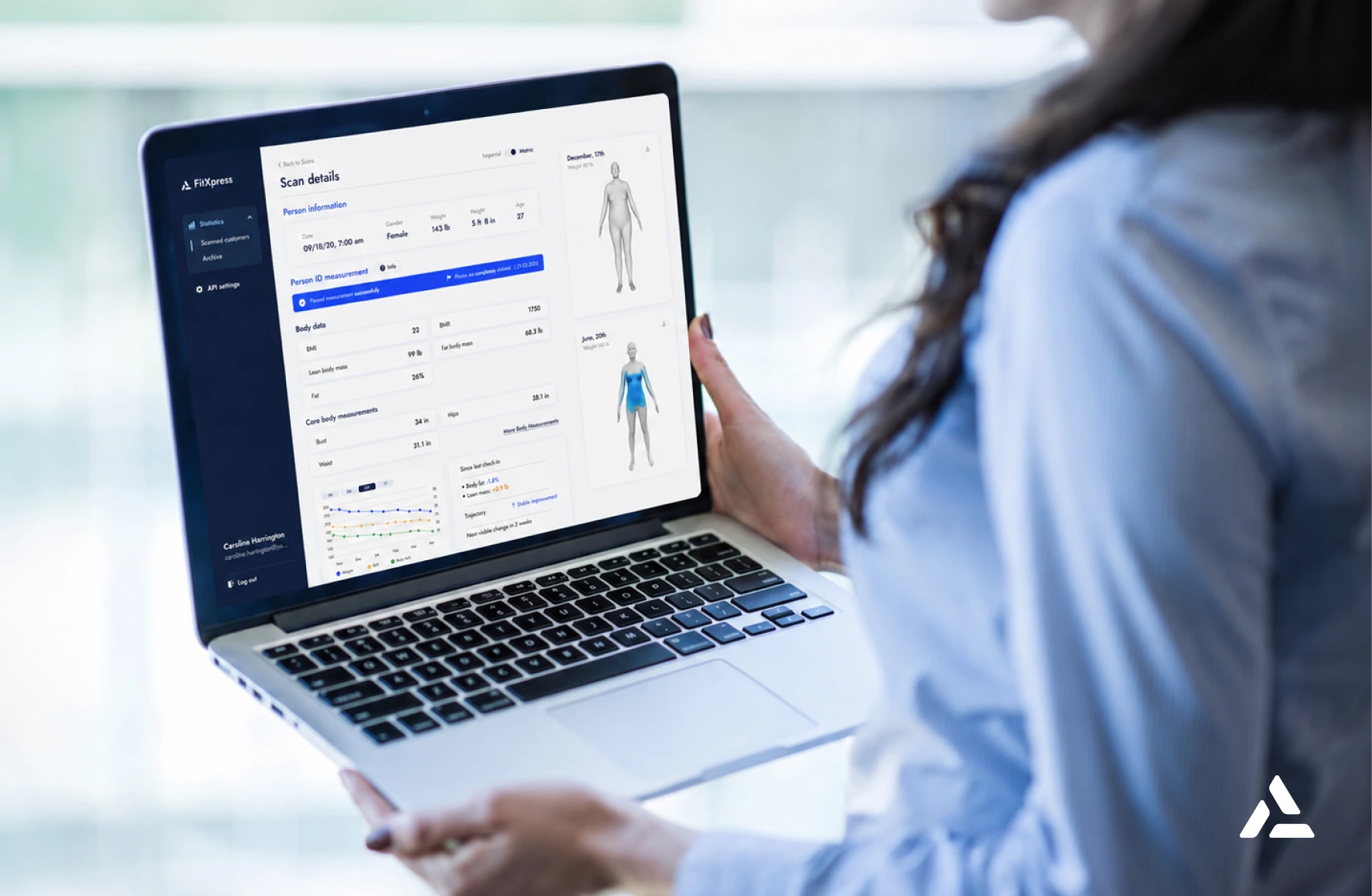 A person holds a laptop displaying a health scan report with body diagrams, charts, and data in a blue and white interface, highlighting the integration of Remote Body Data to enhance the patient experience.